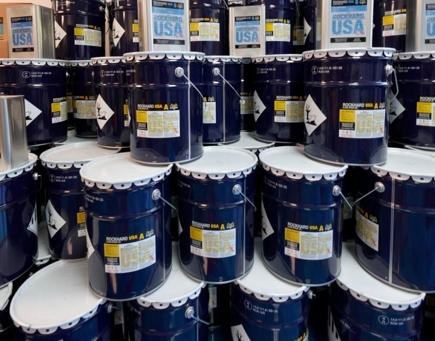 Stacks of blue paint buckets with white lids on store shelves, some labeled USA.