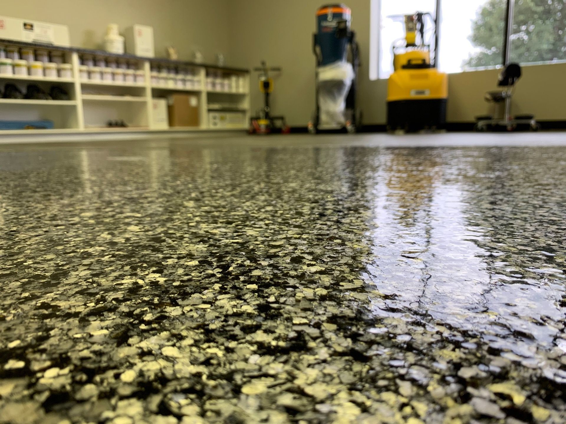Glossy speckled floor in an industrial room with shelves and cleaning equipment in the background