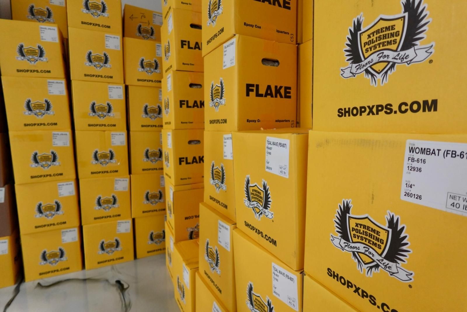 Stacks of yellow SHOPSXPS.COM shipping boxes in a warehouse or storage area.