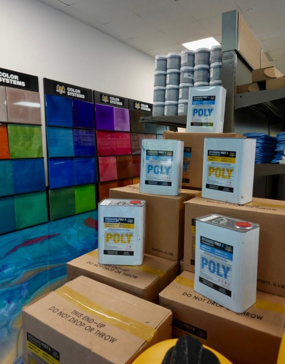 Stacked POLY product boxes in a store aisle beside colorful packaged goods and blue canisters.