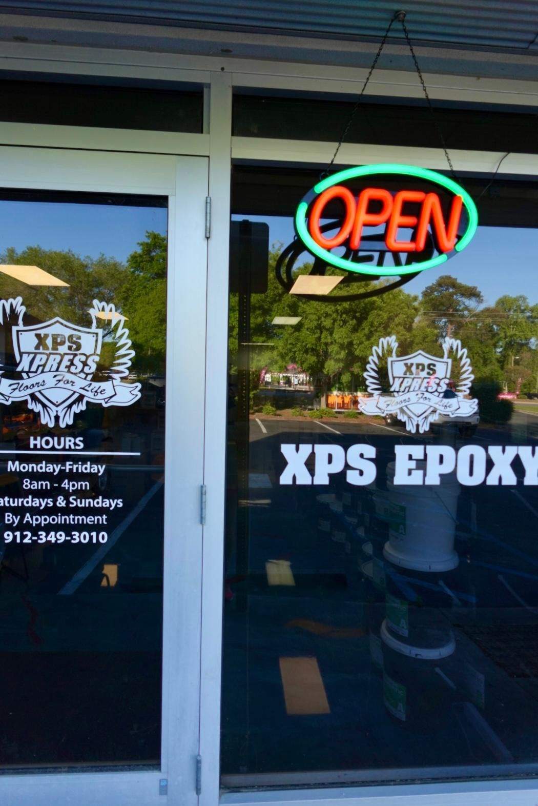 Storefront for XPS Epoxy with neon “OPEN” sign and business hours on the glass door.
