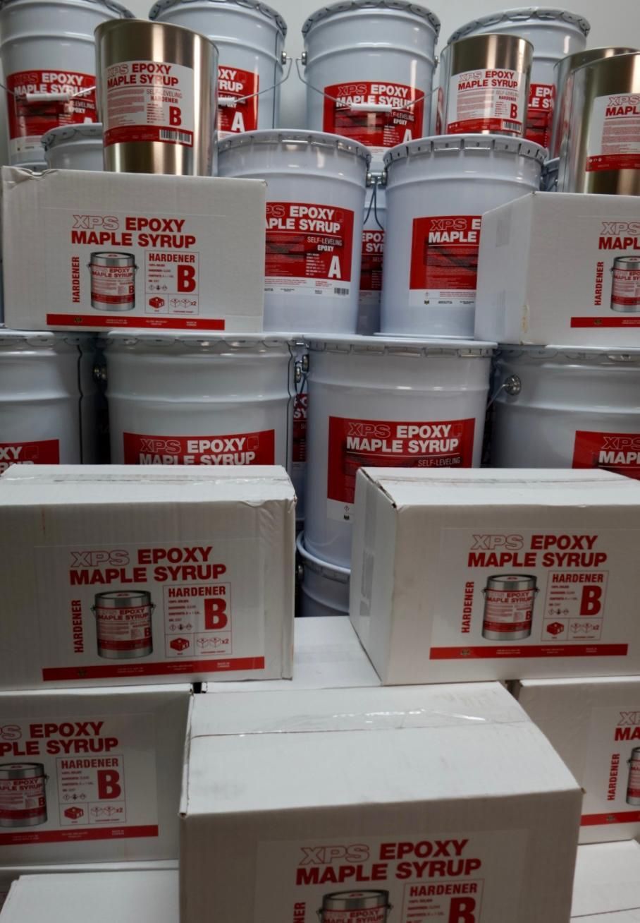 Stacked white epoxy maple syrup pails and boxes with red labels in a store display