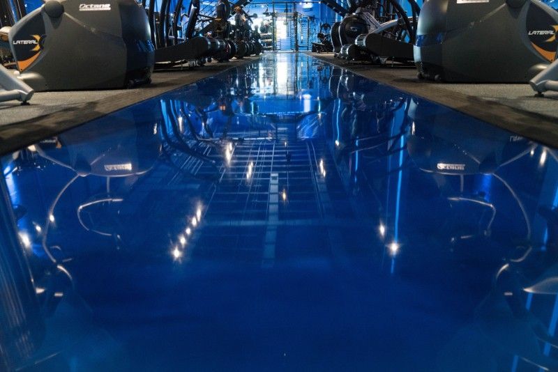 Blue glossy floor reflecting lights in a modern indoor showroom with cars on both sides