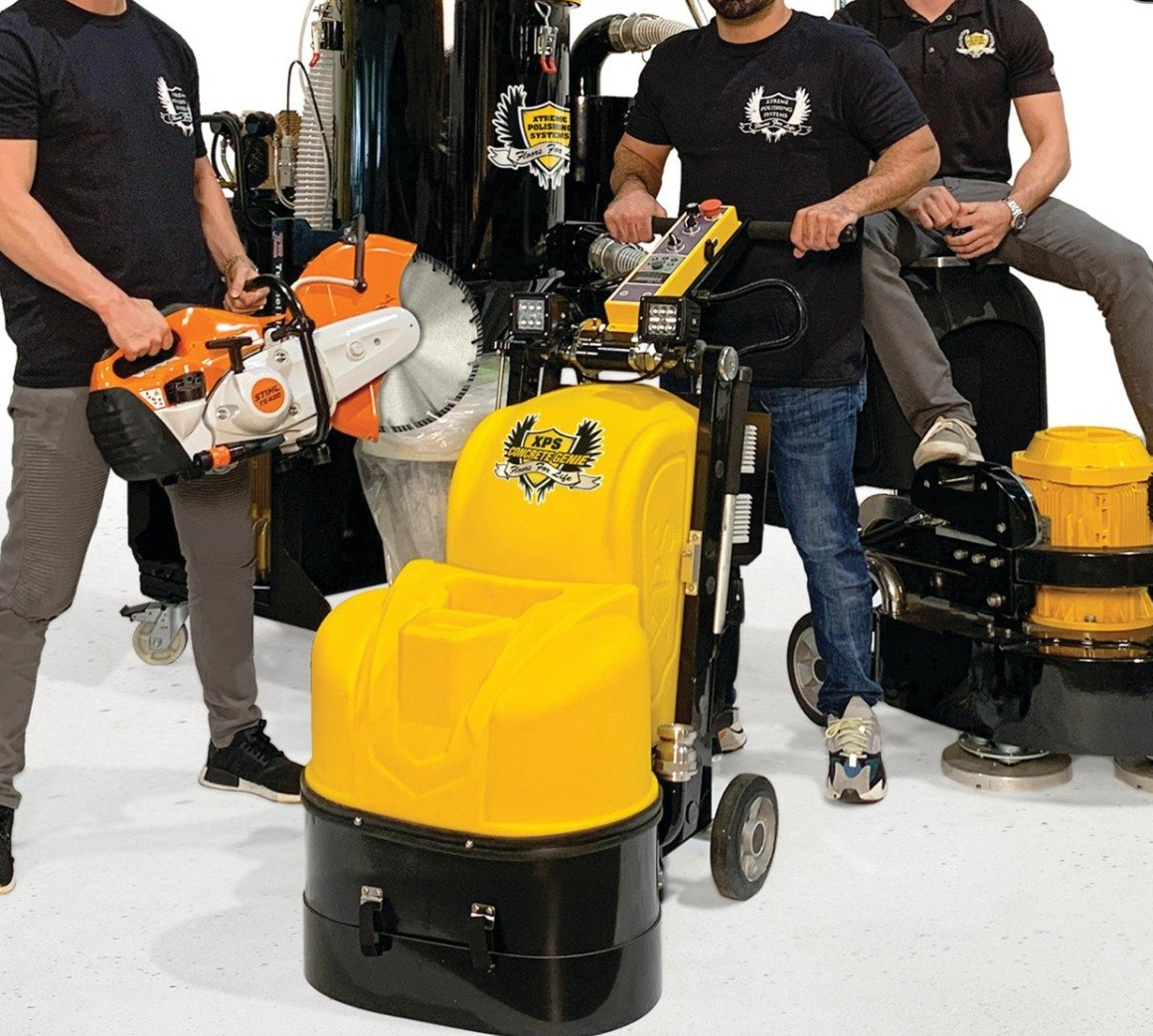 People with floor-cleaning machines in a showroom, including yellow and black models and an orange saw.
