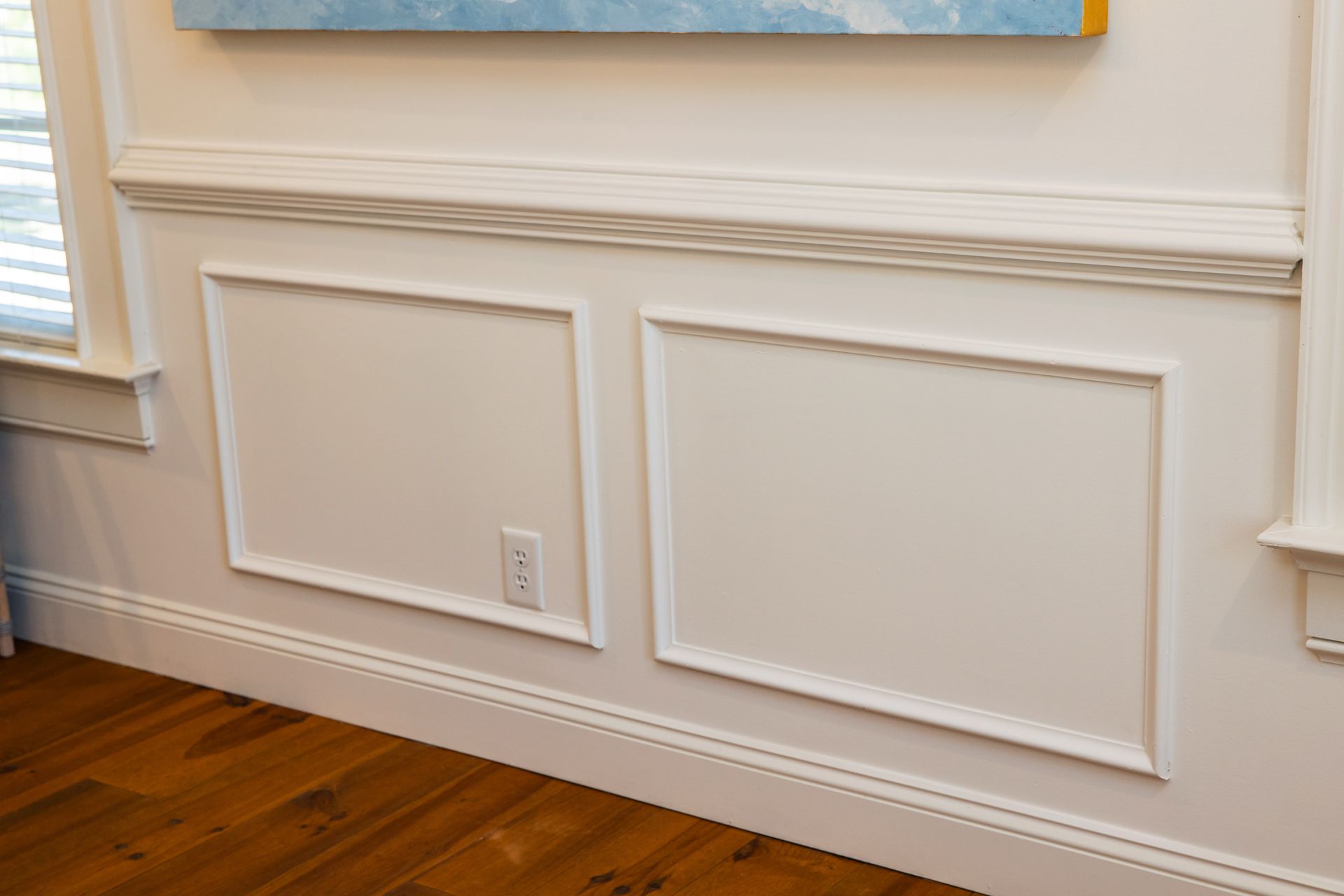 A living room with a painting on the wall and a wooden floor.