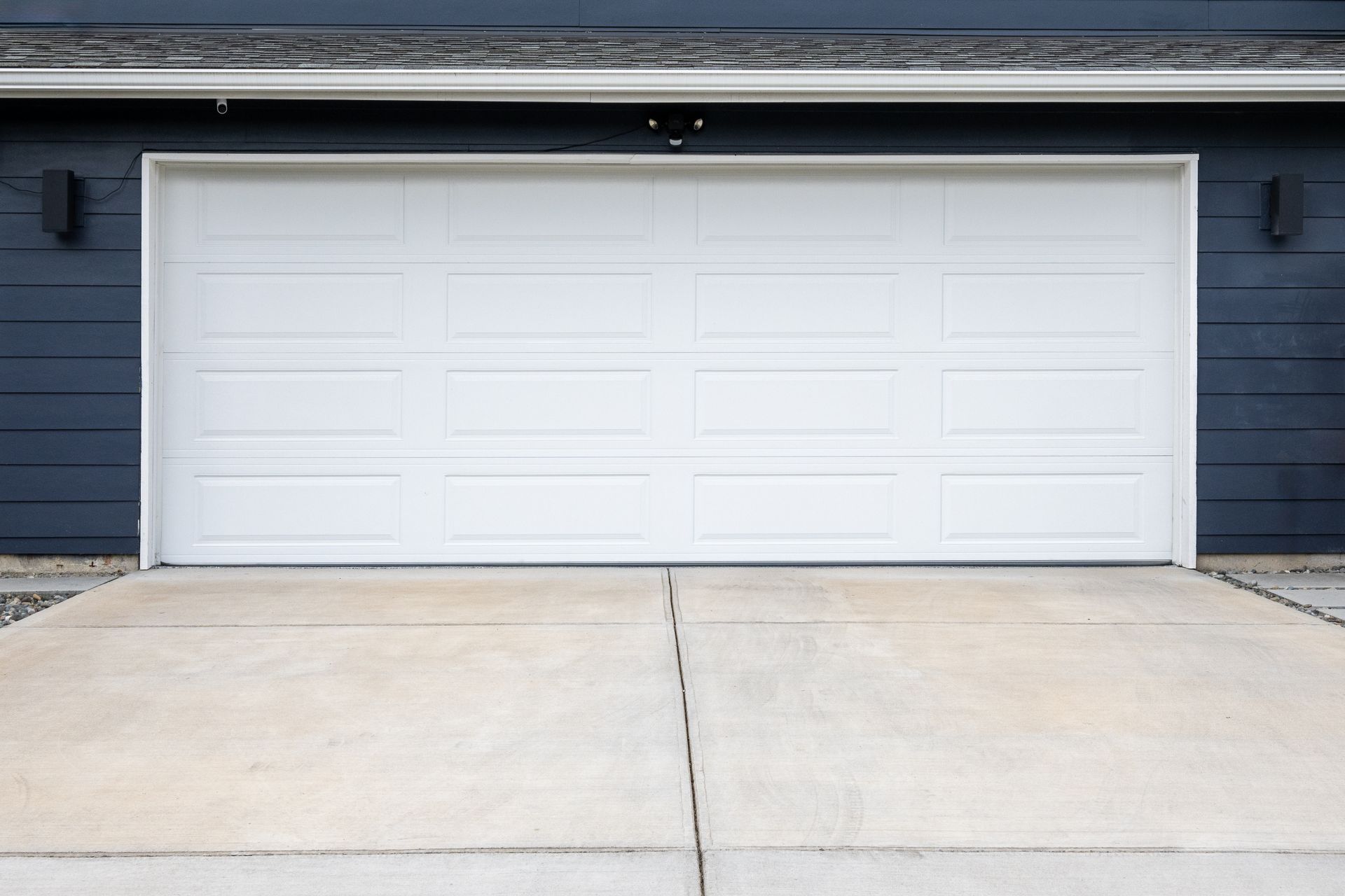 A white garage door is sitting in front of a blue house.