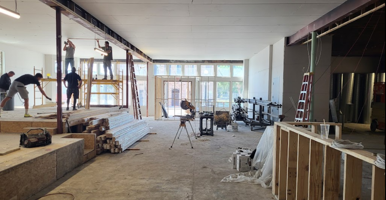 Construction site interior with workers on scaffolding and unfinished walls, floor, and windows