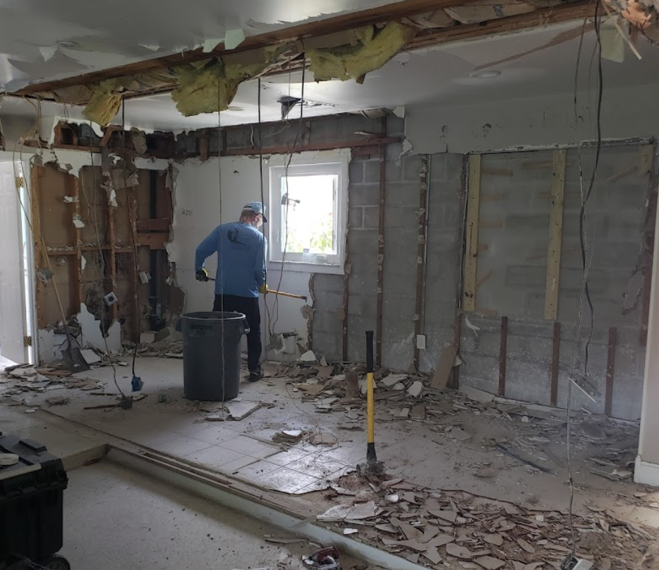 Person working in a room under demolition, with exposed walls, debris, and a window in the background