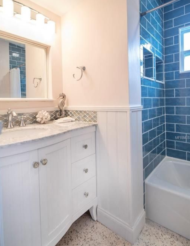 White bathroom vanity with mirror beside a blue-tiled tub and shower.