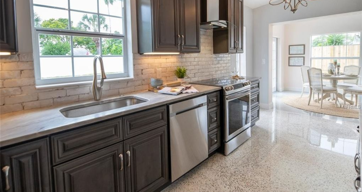 Modern kitchen with dark cabinets, stainless steel appliances, and a bright dining area beyond