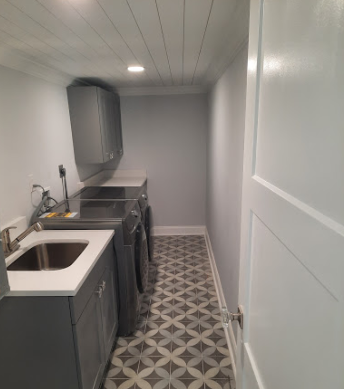 Narrow galley kitchen with gray cabinets, patterned floor tile, and white paneled wall.