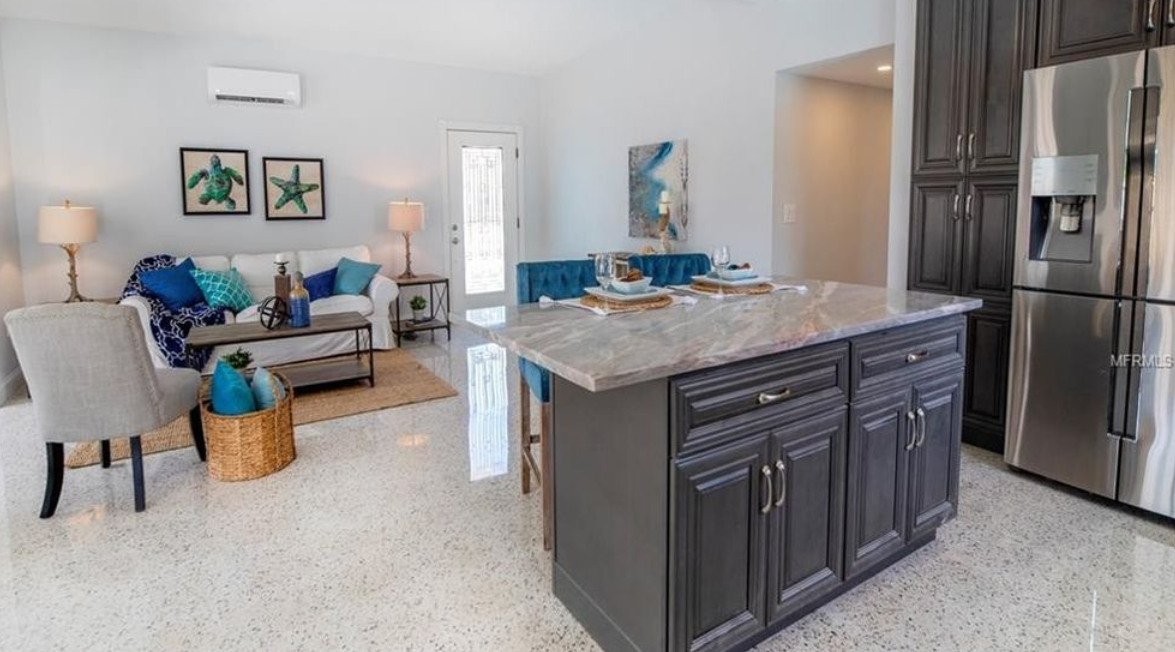 Modern kitchen with dark cabinets and stainless fridge, open to a bright living room with blue accents
