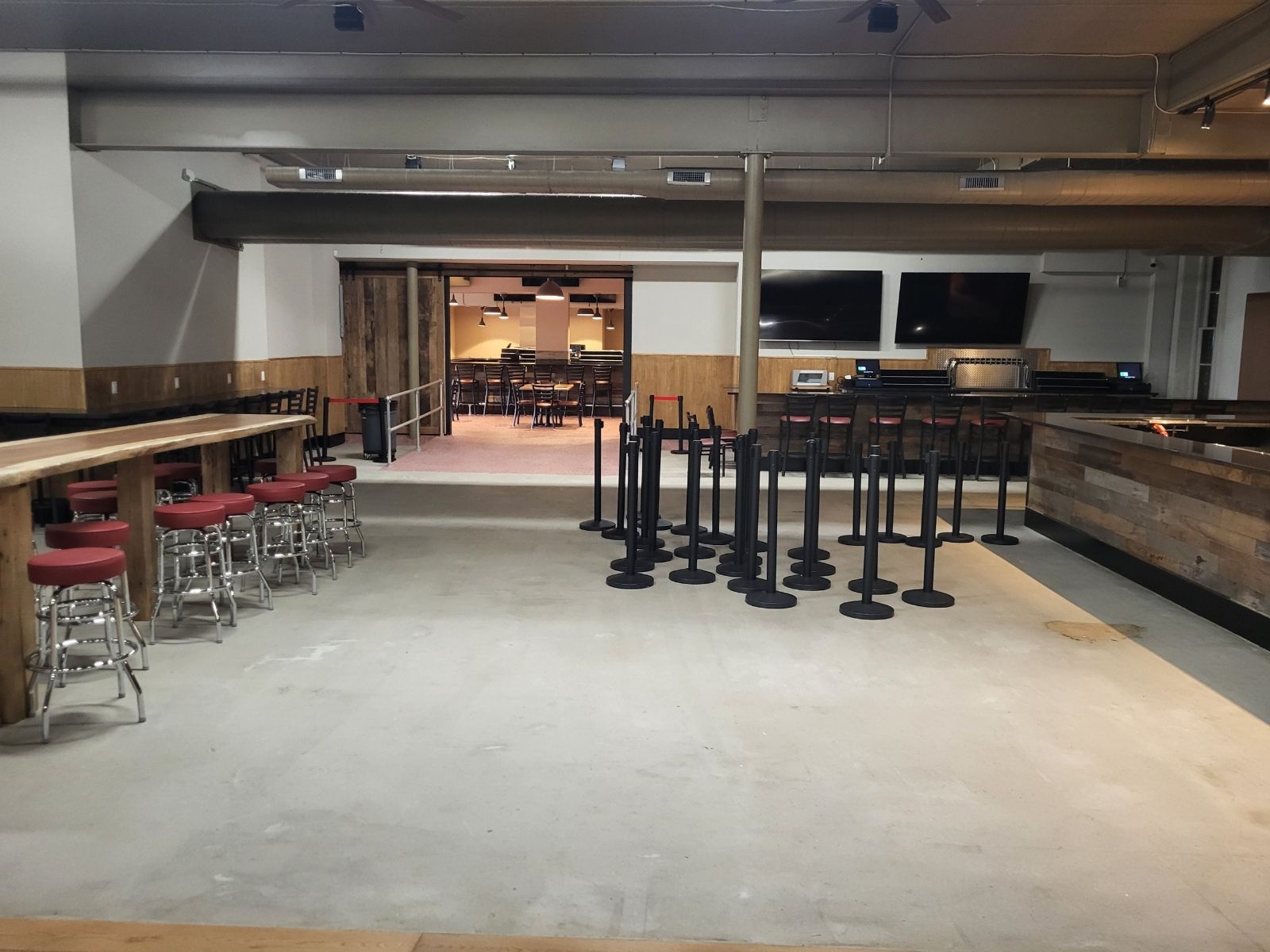 Empty indoor bar with stools, high tables, and stacked chairs in a dimly lit room