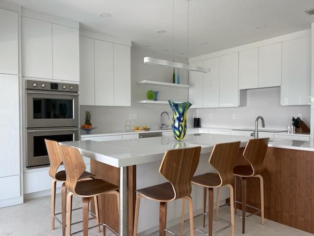 Bright modern white kitchen with wood stools around a marble island and vase of flowers