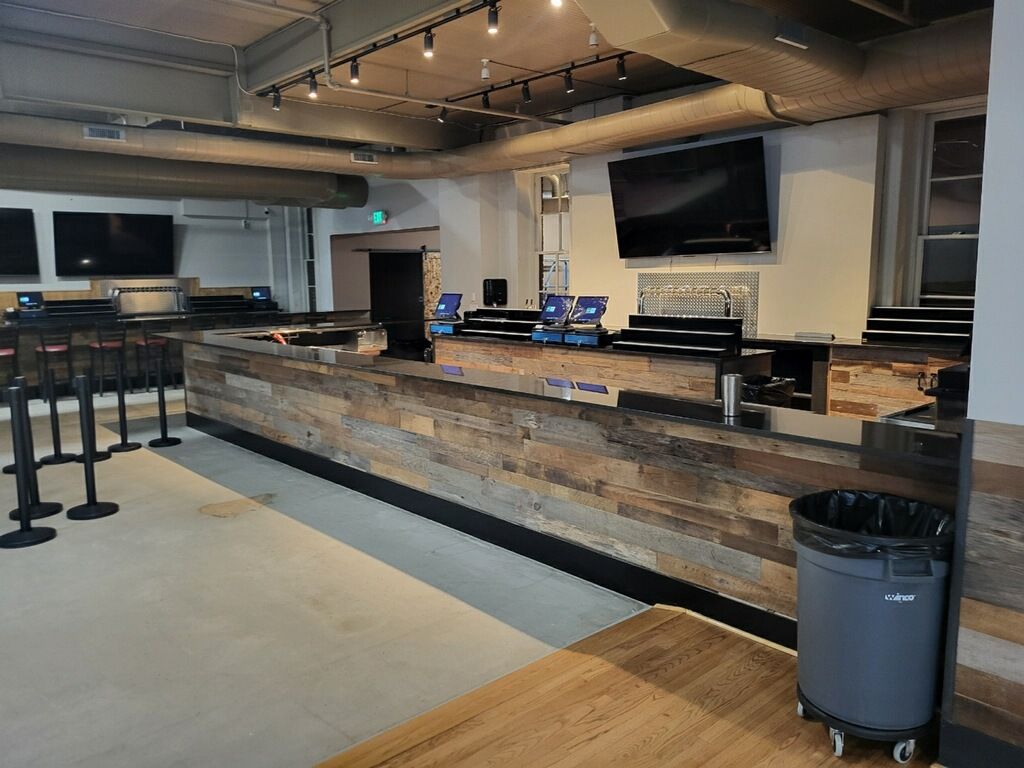 Empty modern café counter with stools, wall-mounted TVs, and a trash can in the foreground.