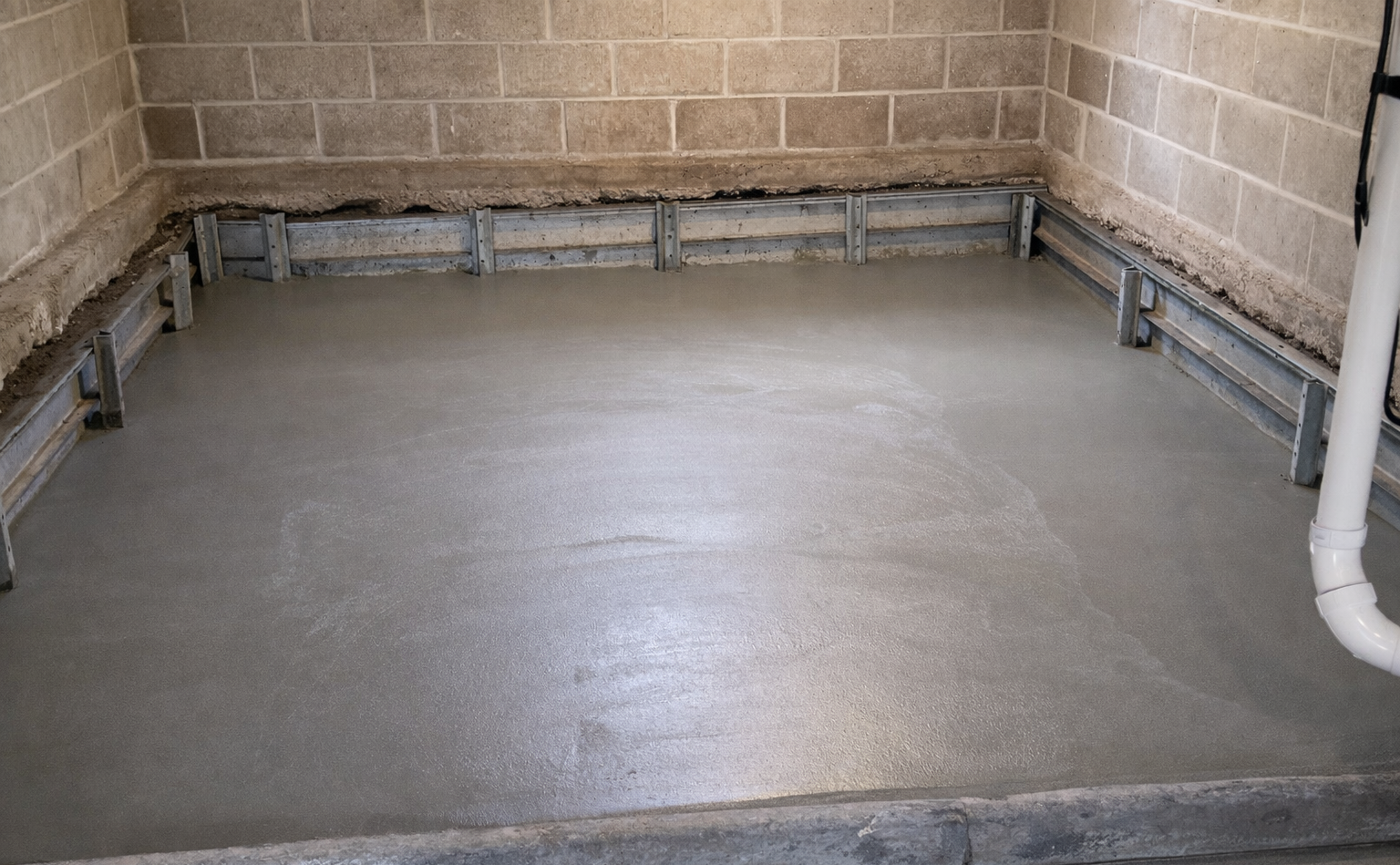 Newly poured concrete floor in a room with cinder block walls; gray and light brown.