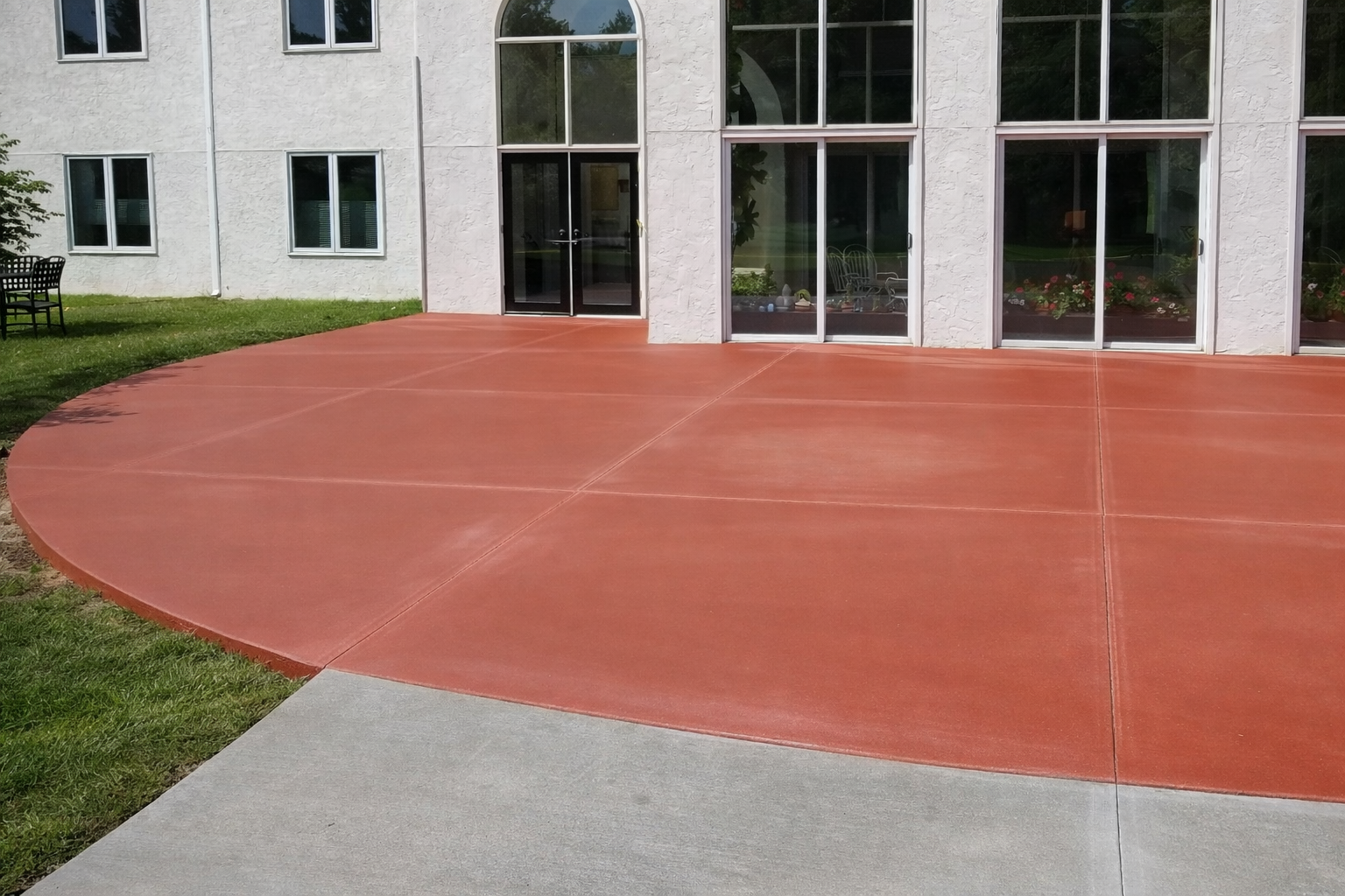 Red concrete patio next to a building with large windows and a grassy area.