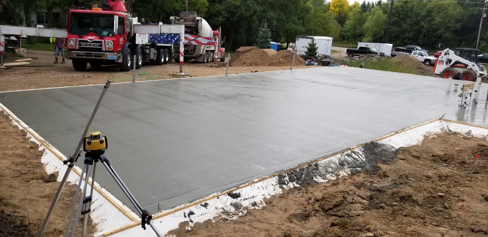 A freshly poured concrete foundation with two concrete trucks, and a leveling device.