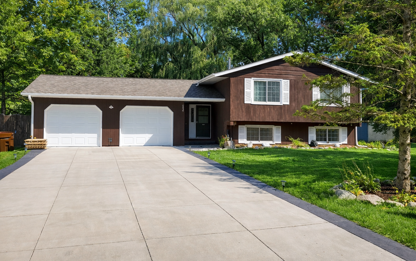 Brown house with white garage doors, driveway, and green lawn.