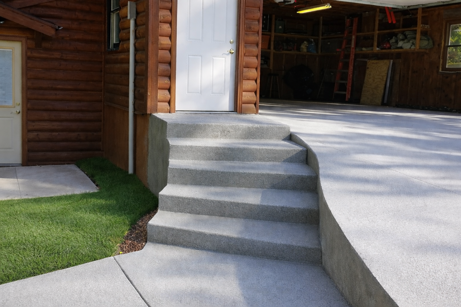 Concrete steps leading up to a white door, next to a building with wood siding.