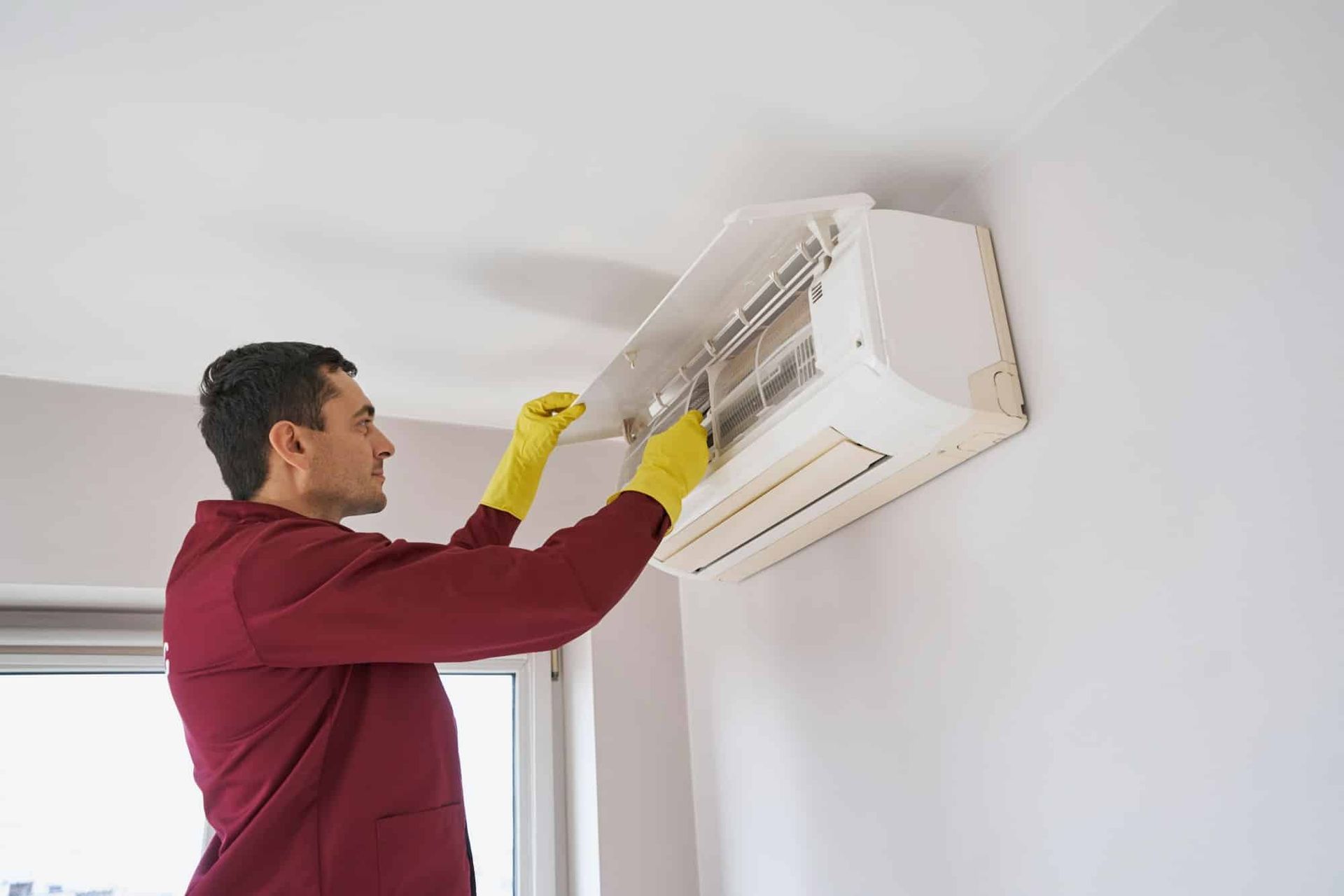 A man wearing yellow gloves is cleaning an air conditioner.