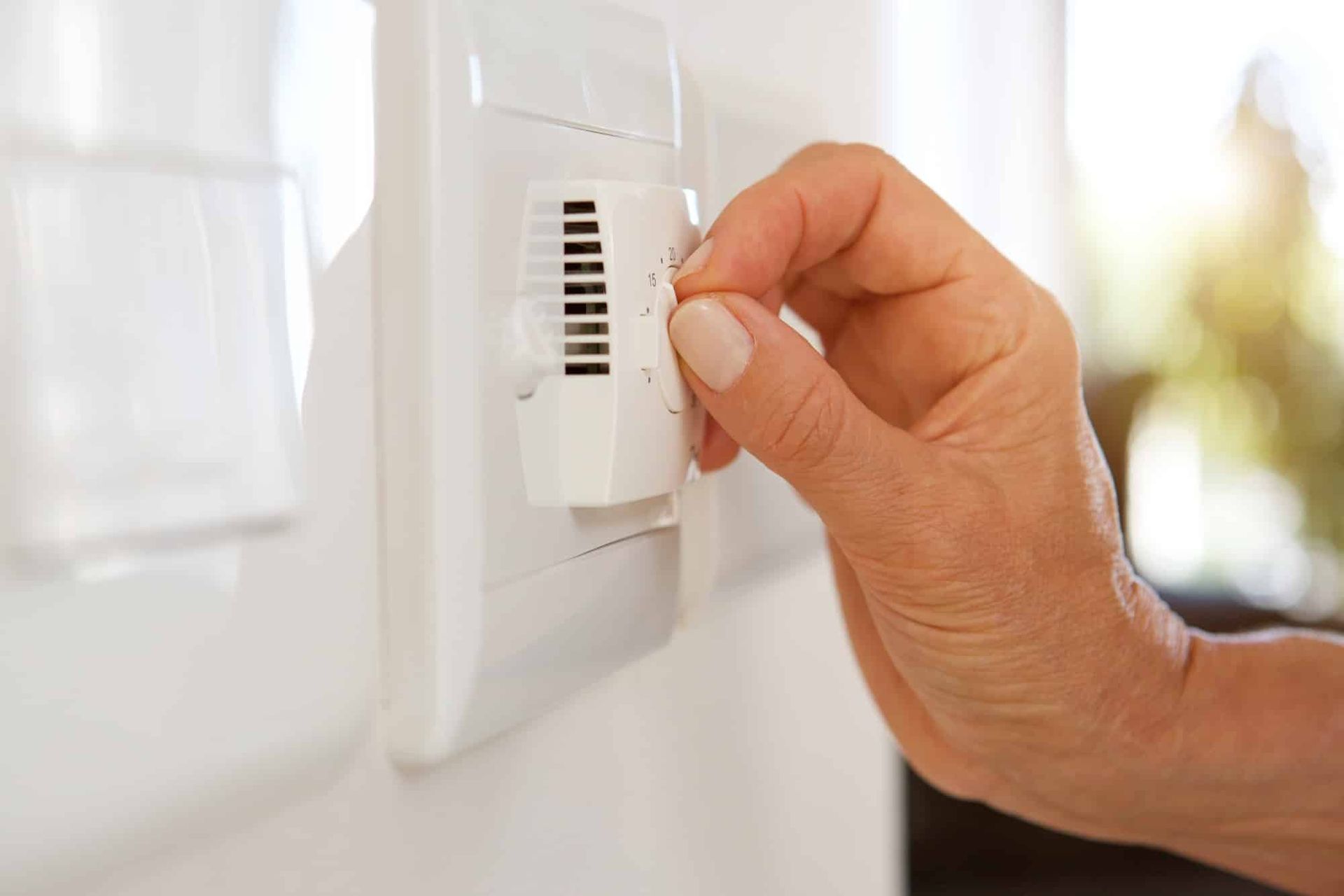 A person is adjusting a thermostat on a wall.
