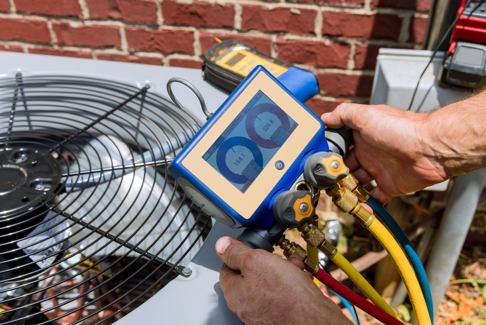 A technician uses digital manifold gauges to measure refrigerant pressures on an outdoor air conditioning unit.
