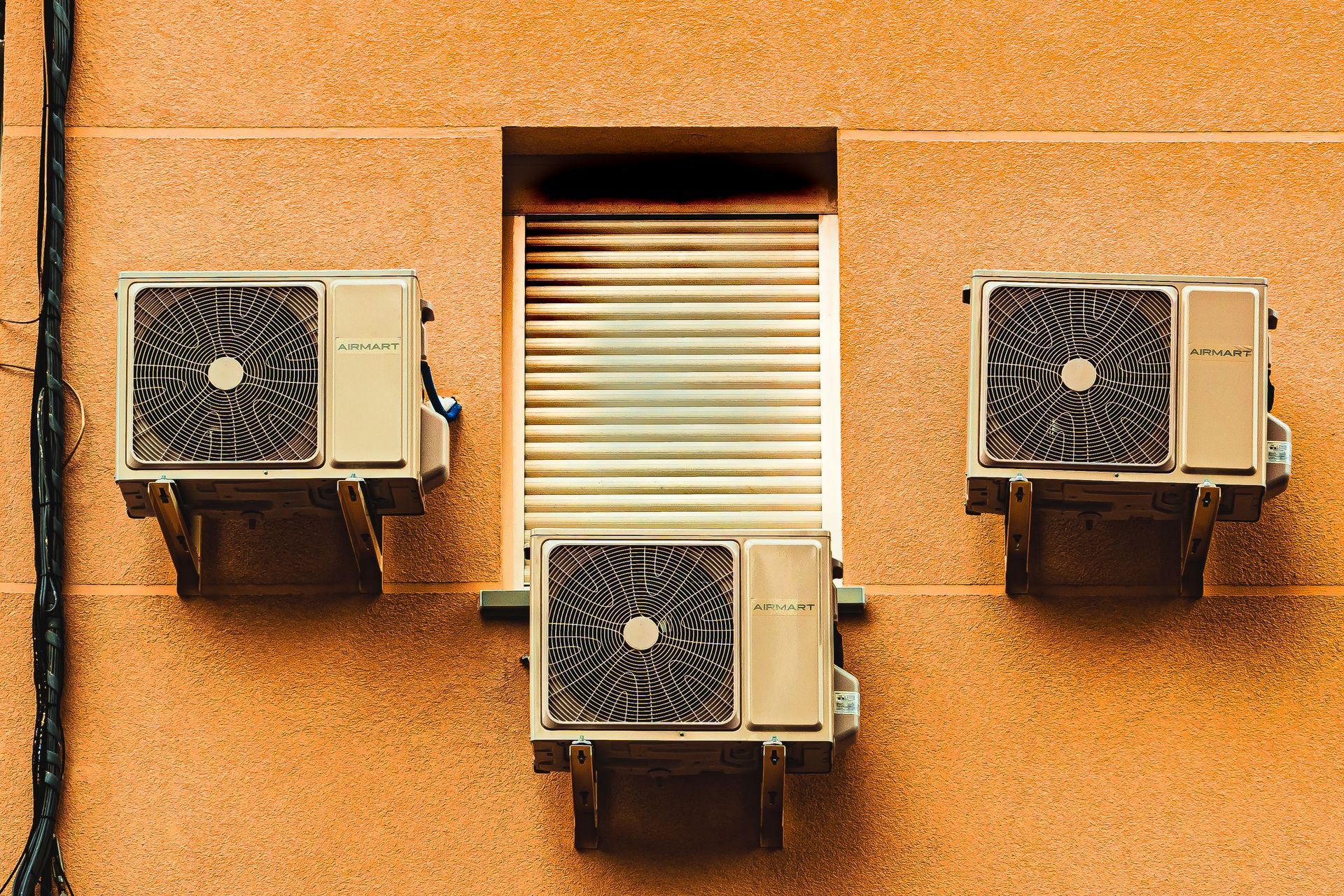 Three wall-mounted air conditioners on an orange stucco building facade.
