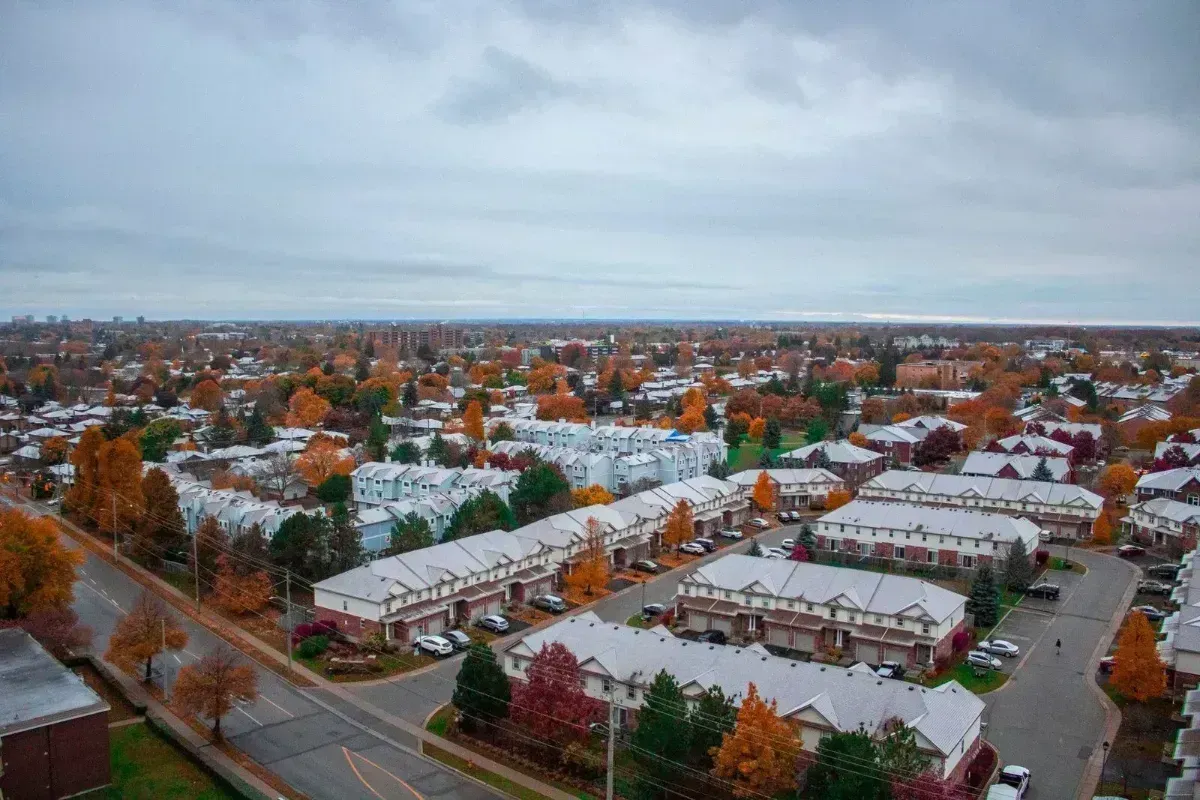Snow-covered suburban neighborhood with rows of houses under a cloudy sky.