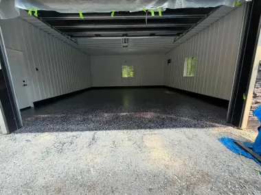 Empty shipping container with white walls, black floor coating, and open doors in a storage area