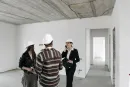 Three people in hard hats discussing plans inside an unfinished building.