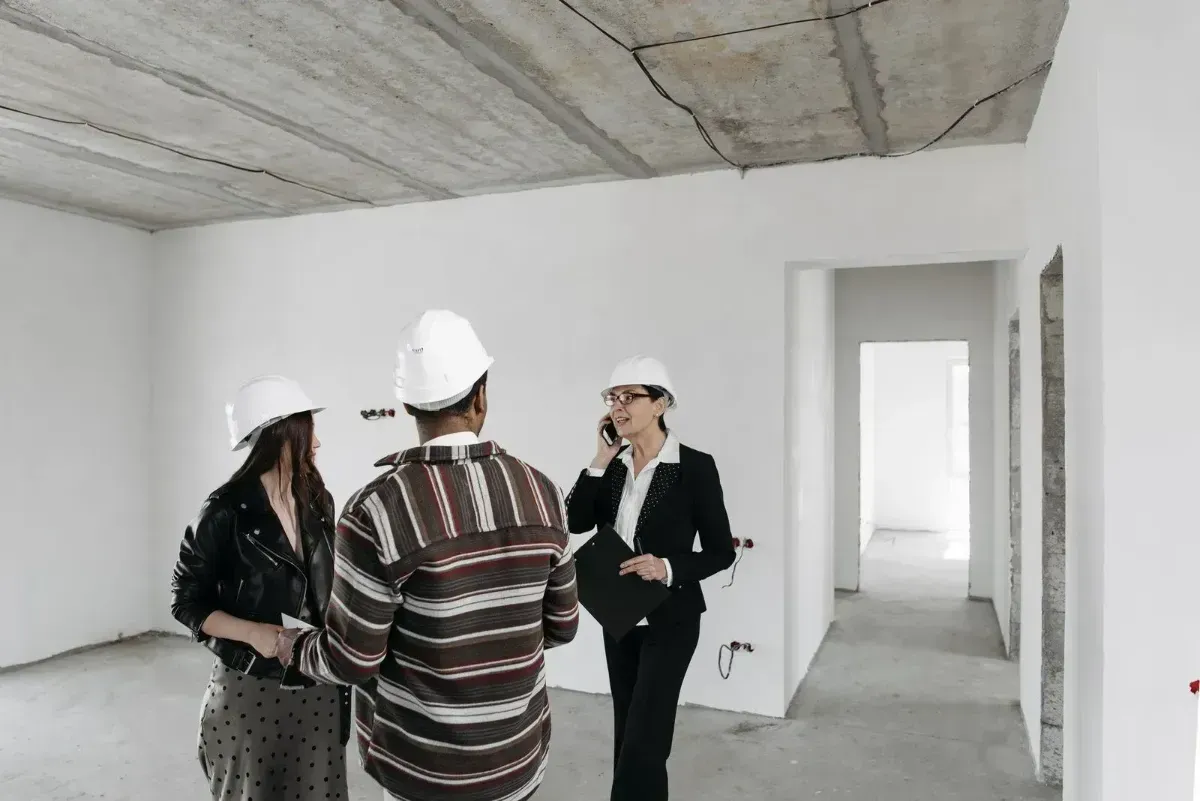 Three people in hard hats discussing plans inside an unfinished building.