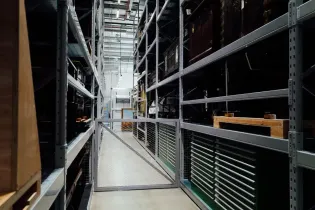 Warehouse aisle with tall metal shelving and stacked storage bins, lit by bright overhead lights