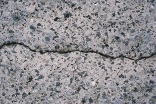 Close-up of a cracked gray concrete surface with dark speckles