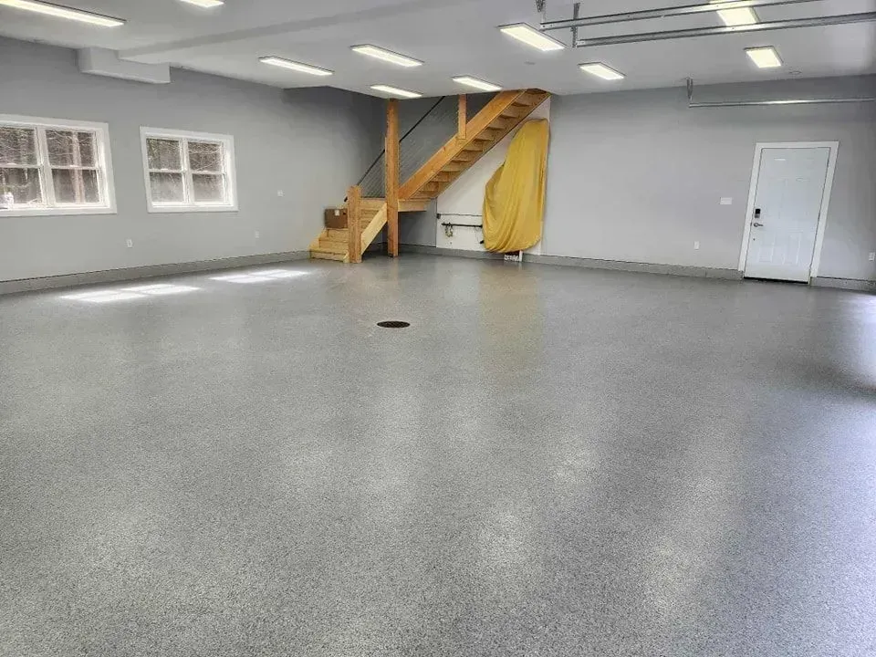 Empty gray garage-like room with a wooden staircase and small windows along the wall.