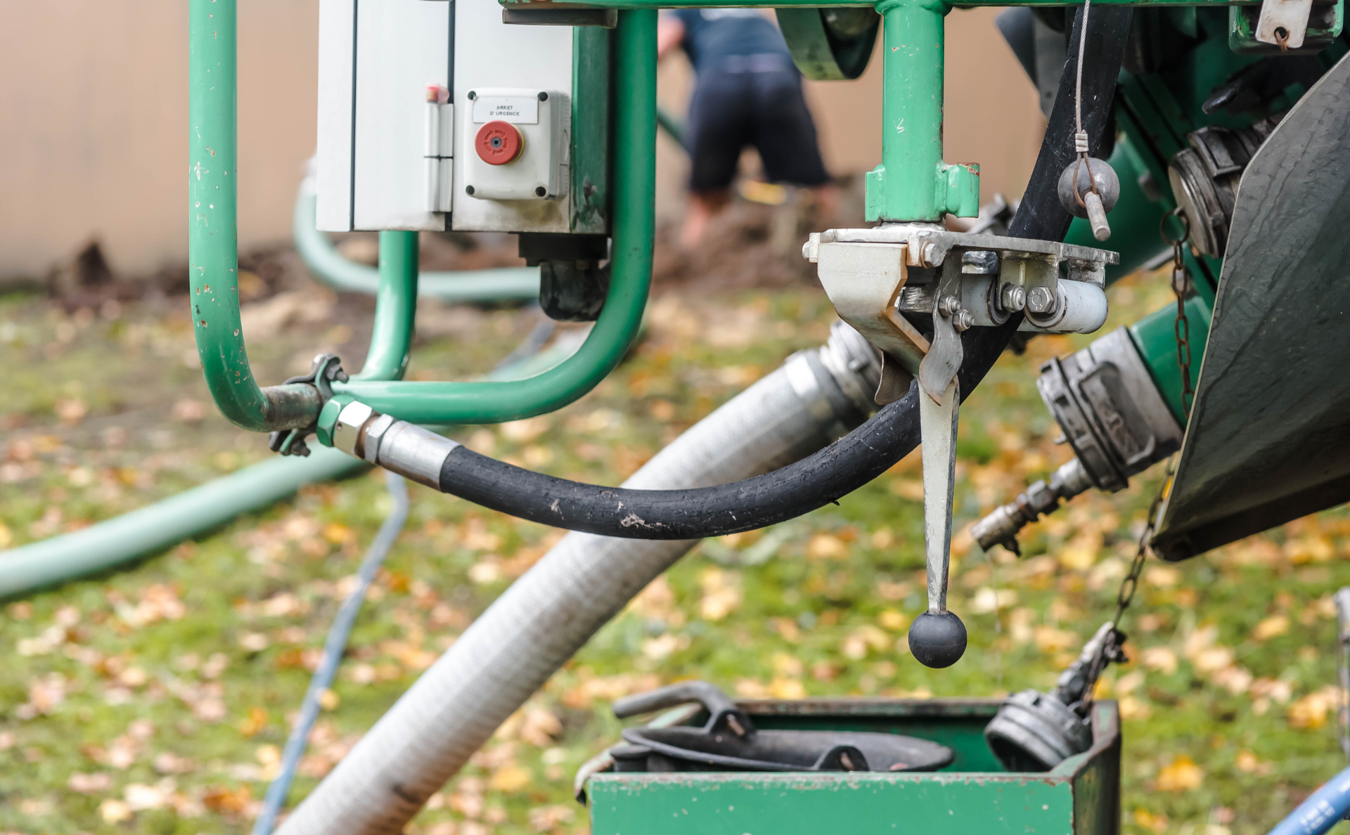 A close-up of green industrial equipment, featuring a control box with a red button, hoses, and a metallic lever.