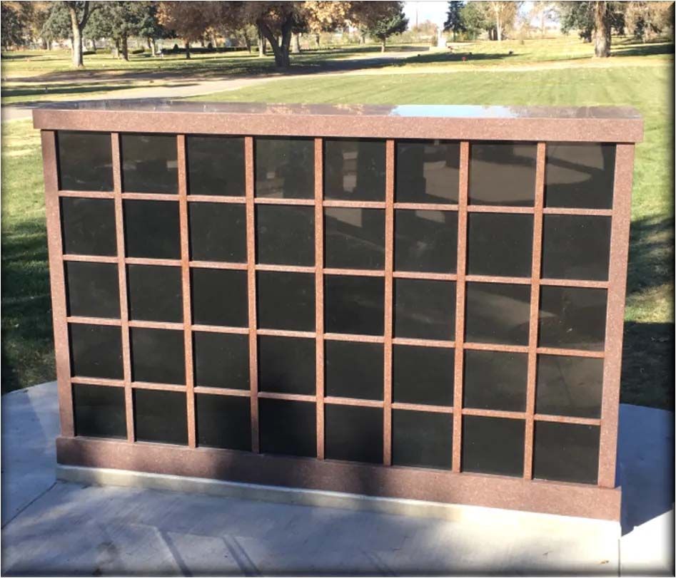 Bronze columbarium with multiple compartments on a concrete base, set in a grassy park.