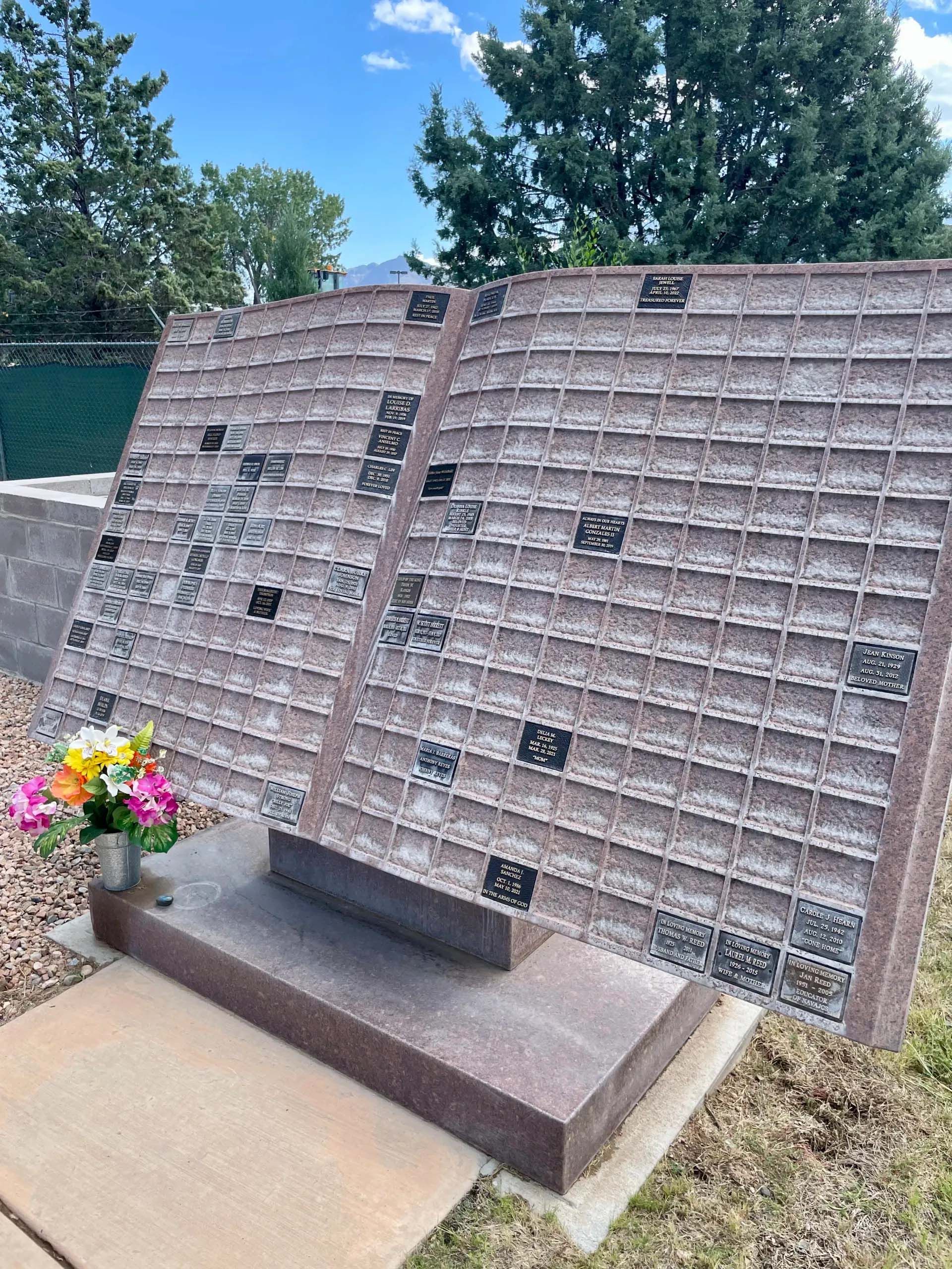 Monument in a cemetery with a book-like design, holding many small memorial plaques.