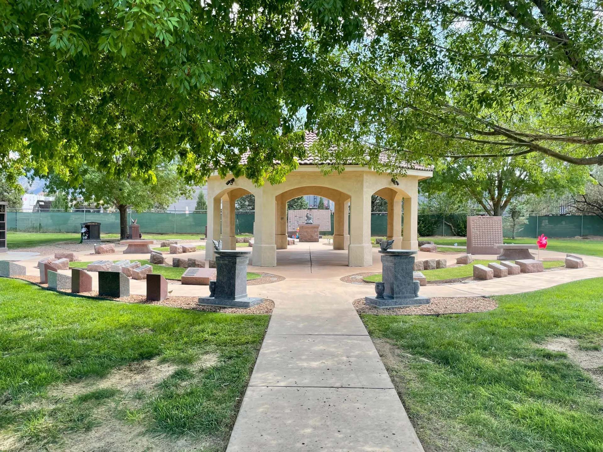 Park with a gazebo, stone benches, and walkway. Trees provide shade on a sunny day.