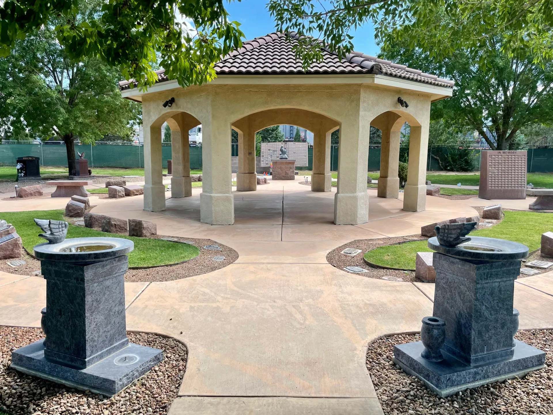 Gazebo in a memorial garden with stone markers and a water feature; blue sky, green grass.