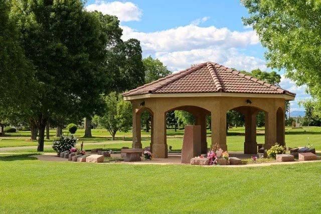 A gazebo in a cemetery, surrounded by green grass and trees, under a blue sky.