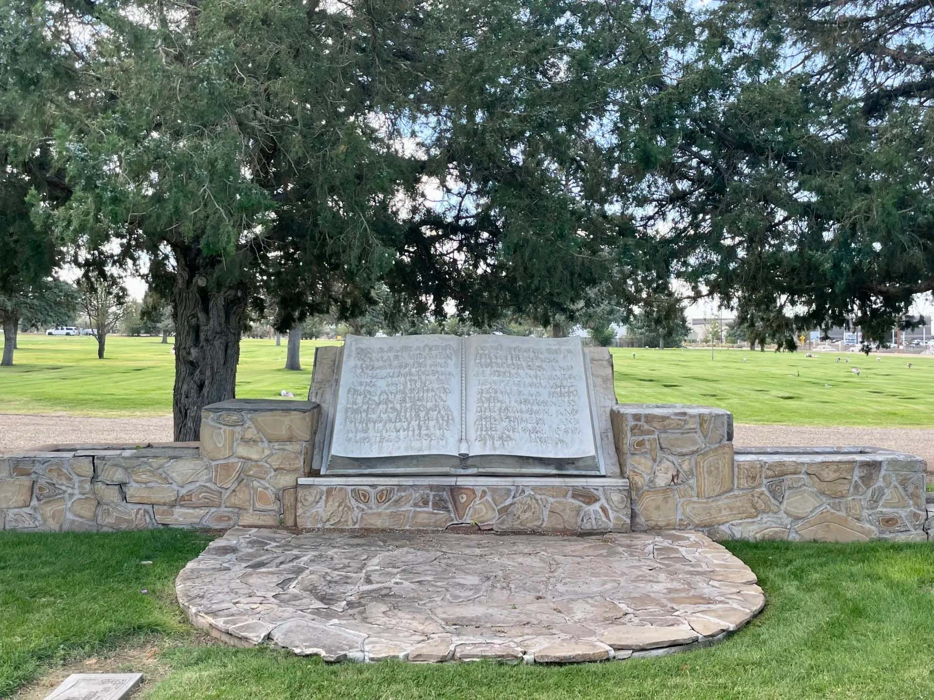 Stone monument in a grassy park, resembling an open book, with text and a stone base.