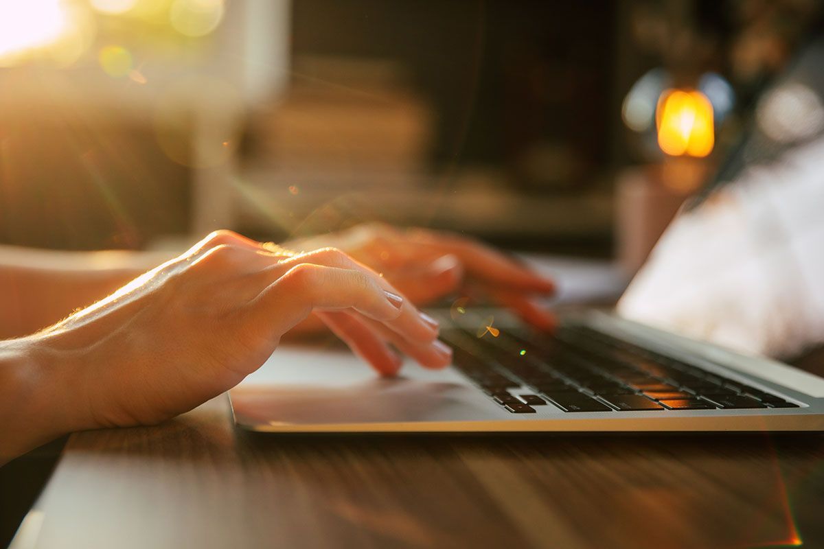 Hands typing on a laptop keyboard, lit by warm sunlight.