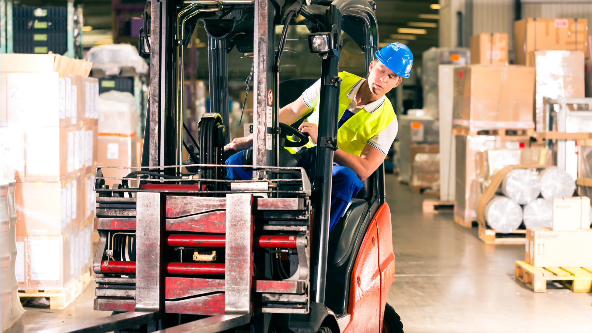 Forklift operator in blue hard hat moving pallets in a warehouse aisle