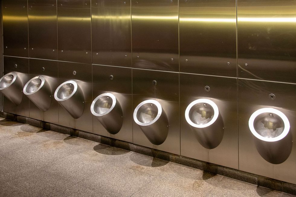Row of stainless steel urinals in a tiled restroom, lit by warm yellow lights.