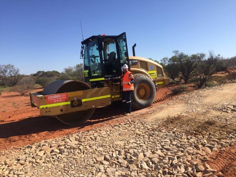 A man is standing next to a yellow bulldozer on a dirt road.