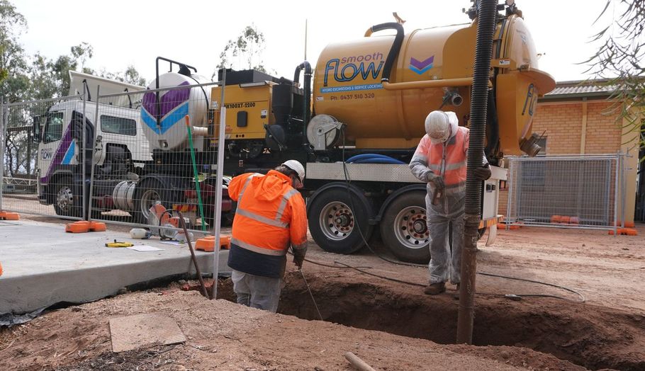 Two men are digging a hole in front of a truck that says flow