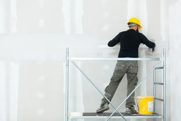 Finisher on scaffolding plastering a drywall.