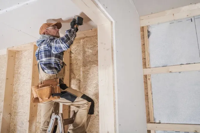 Contractor installing drywall near a doorway.