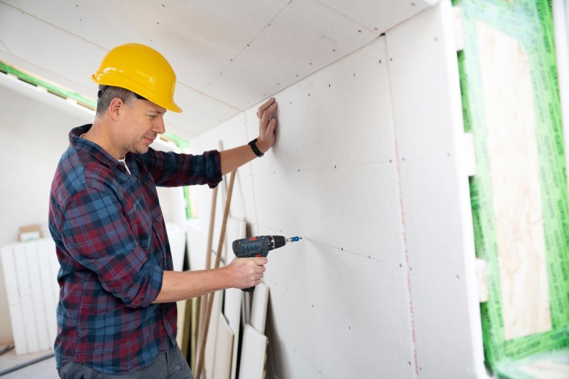 Professional installing drywall using a drill.